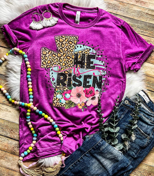 Magenta tee with leopard cross, flowers, and the words he is risen.